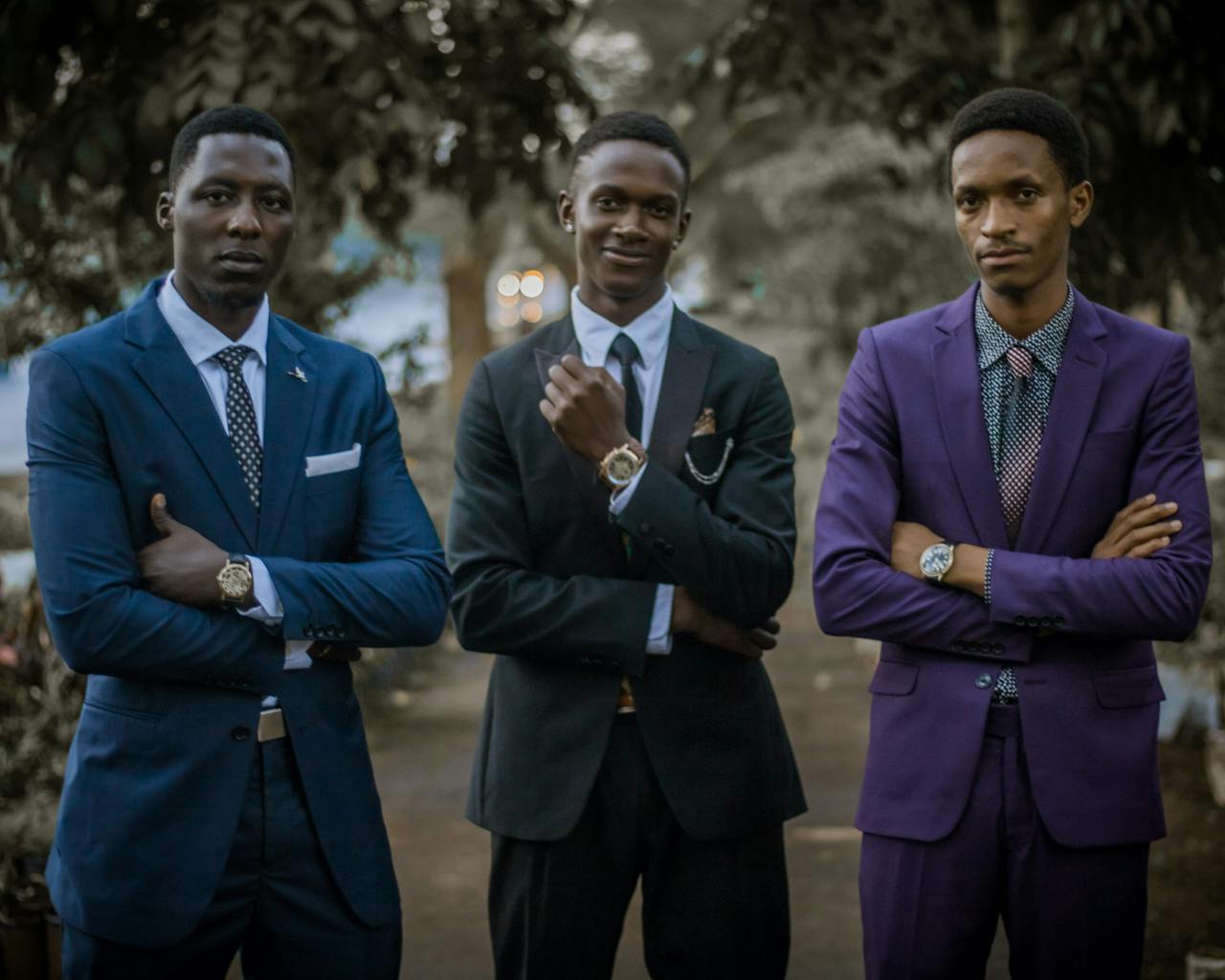Three young men in elegant suits posing confidently outdoors.