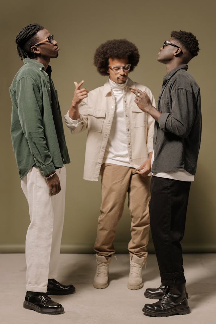 Home Three men in trendy outfits pose confidently on a neutral backdrop, showcasing modern fashion.